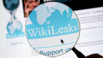 Wikileaks logo i ett förstoringsglas, i den suddiga bakgrunden Julian Assange.