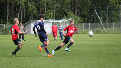 Tre killar springer efter bollen på en fotbollsplan. Killen i röd tröja till höger är Robert Bäckman från Hangö.