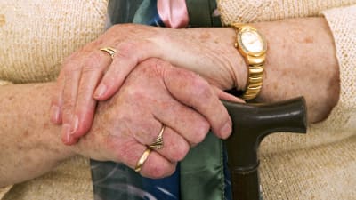 En äldre persons händer på en käpp.