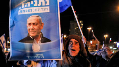 En man håller i en valplansch med ett foto på Israels premiärminister Benjamin Netanyahus  ropar slagord