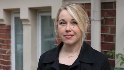 En blond kvinna står framför en tegelvägg.
