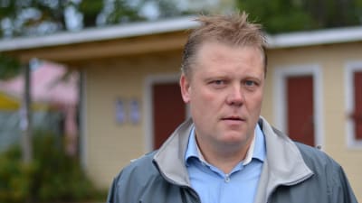 Man står framför en låg gul träbyggnad.