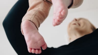 Nuori äiti nostaan vauvaansa ilmaan ja hymyilee hänelle.