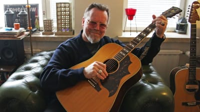 Neumann med en akustisk Gibson gitarr i sitt vardagsrum