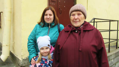 Tre kvinnor i Sankt Petersburg från tre olika generationer poserar vid ett gult stenhus. 