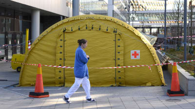 Ett gult tält utanför Karolinska universitetssjukhuset och en sjukskötare som går förbi. 