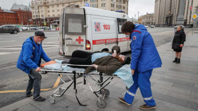 Ambulanspersonal tog hand om en äldre kvinna som kollapsade vid en busshållplats i centrum av Moskva i fredags. Det är oklart vad kvinnan led av. 