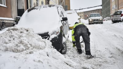 En man skottar snö för att komma loss med bilen i berghäll i Helsingfors tisdagen den 29.1.
