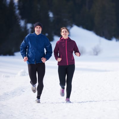 Två personer som ser glada ut, ute på en löprunda i snöigt landskap.
