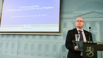 Justitie- och arbetsminister Jari Lindström i talarstol med finländsk lejonlogo.
