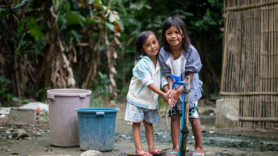 två filippinska flickor tvättar händerna vid en vattenpost