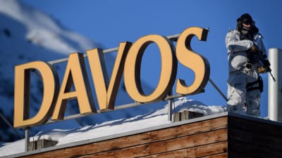 Beväpnad polis i vintermundering på snöklätt tak och skylt med ortsnamnet Davos.