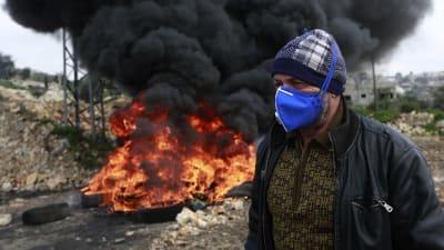 En palestinsk demonstrant passerar en brinnande barrikad utanför en israelisk bosättning nära staden Nablus på Västbanken.