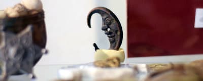 Ett gammalt metallföremål som ser ut som en måne med ansikte står utställd i en monter på ett museum.
