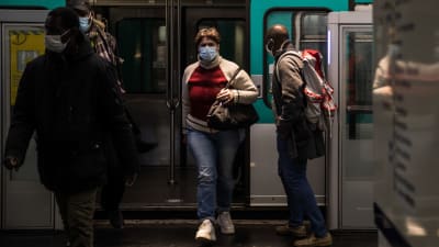 Passagerare kommer ut ur en metro i Paris. De har munskydd på sig.