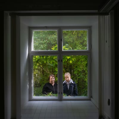 Outi Paltta ja Eila Kotkamaa kuvattuna ikkunan läpi Huvituksen kartanon puutarhassa Yläneellä. 