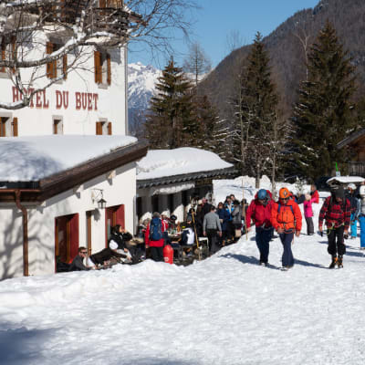 Människor i vinterkläder är samlade runt en vit byggnad. Det är snö på marken och i bakgrunden skymtar ett högt berg.