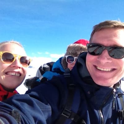 Tuomas Heikkilän perhe hiihtämässä Italian Alpeilla, taustalla sininen taivas ja vuoristomaisemaa.