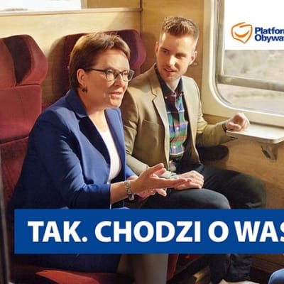 Perhe matkustaa junassa ja pääministeri Ewa Kopacz juttelee heidän kanssaan.