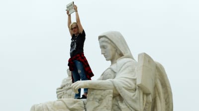 En demonstrerande kvinna har klättrat högt upp i famnen på en staty utanför USA:s högsta domstol i Washington DC