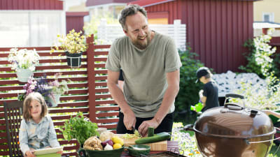 Anders Samuelsson utomhus i solen framför ett bord med fräsha grönsaker och rotsaker.