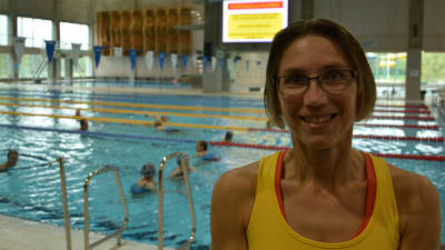 Susanna Vuori, en dam med en gulröd topp och glasögon, står vid en simbassängskant.