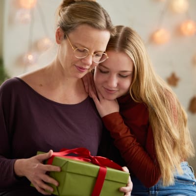 Äiti ja teini-ikäinen tyttö katsovat lahjapakettia.