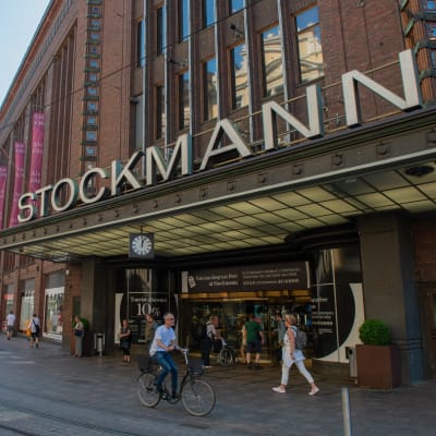 Stockmanns byggnad i Helsingfors. Människor går och cyklar förbi.