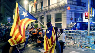 Man invirad i katalansk flagga kastar orangefärgad plastboll mot polis.