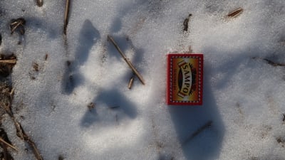 Ett tassavtryck av varg i snö och intill ligger en tändsticksask
