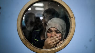 Palestiinalainen nainen katsoo sairaalan oven ikkunan läpi itkien haavoittuneita.