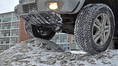 Närbild på terrängbil där däcken är uppkörda på en snöhög.