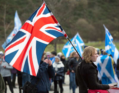 En demonstrant står med en brittisk flagga på axeln. Bakom honom syns flera demonstranter med skotska flaggor.
