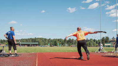 Mies heittää litistettyä kumisaapasta urheilukentällä kesällä.
