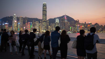 Turister tittar på solen som går ner bakom Hong Kong vid Victoria Harbour. 