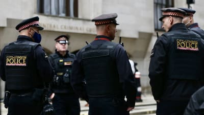 Poliser i London står med ryggen mot kameran. På deras rygg står "City of London police". De är klädda i uniform.