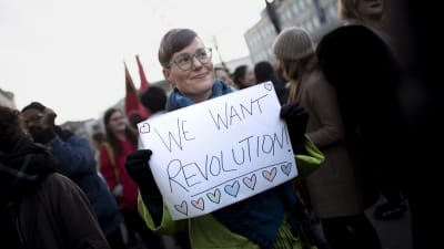 En kvinna håller upp en skylt med texten "We wan't revolution" på en demonstration i Berlin.