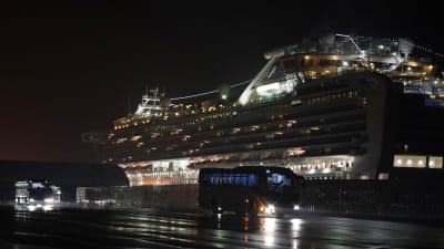 Buss framför kryssningsfartyget Diamond Princess i hamnen i Yokohama, Japan. Bilden är tagen på kvällen så det är mörkt på bilden.