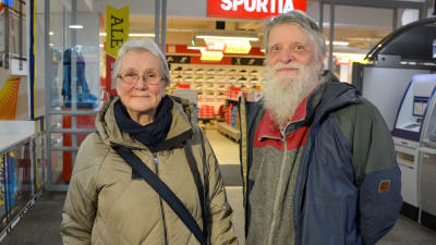 En kvinna och en man står bredvid varandra och tittar in i kameran. De är båda gråhåriga och klädda i vinterkläder.
