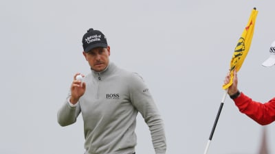Henrik Stenson med en golfboll i handen och en gul flagga bredvid sig.