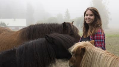 Sabina Granbacka tillsammans med sina tre hästar. Alla hästar står runt henne, med ansiktet mot henne.