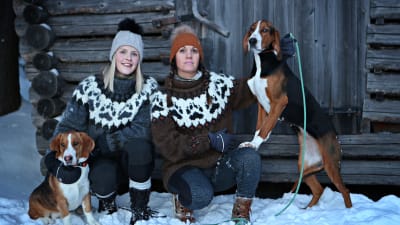 Lina och Marina i snön framför en lada tillsammans med två hundar.