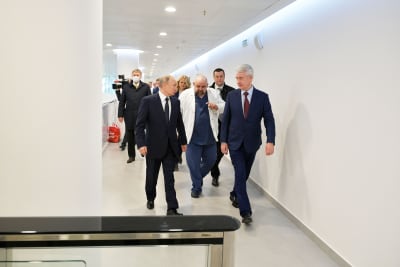 Putin och Sobjanin går i en vit korridor, följda av en läkare i vit läkarrock och en massa människor. 