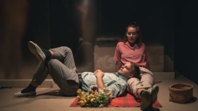 En man ligger på golvet med huvudet i en kvinnas knä. 