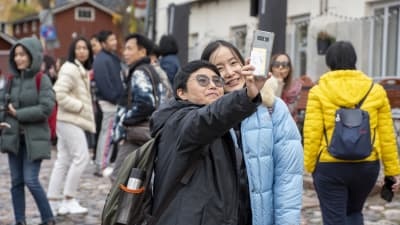 Två thailändska kvinnor tar en selfie på ett torg.