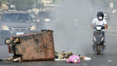 En mopedist kör förbi en brinnande avfallscontainer på en gata i Beirut.