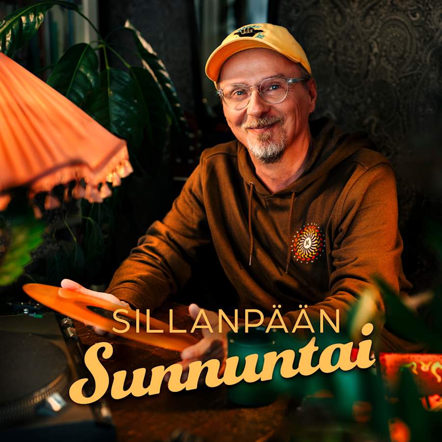 Kuvassa henkil� istuu, pit�� k�siss��n vinyylilevy� ja katsoo kameraan hymyillen.