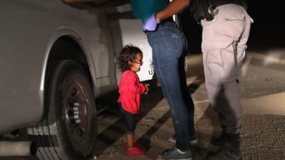 Ett barn från Honduras gråter då hennes mor kroppsvisiteras vid gränsen mellan USA och Mexiko