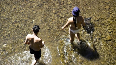 Två människor svalkar sig i en flod som endast räcker upp till deras fotled. 