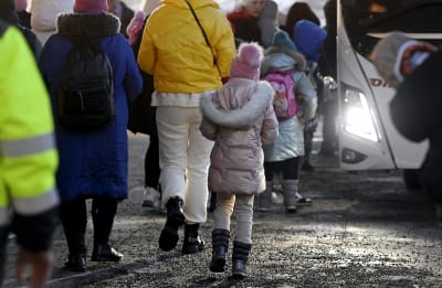 Ukrainska flyktingar i vinterklädsel promenerar med ryggen mot kameran på Busholmen i Helsingfors den 16 mars 2022.